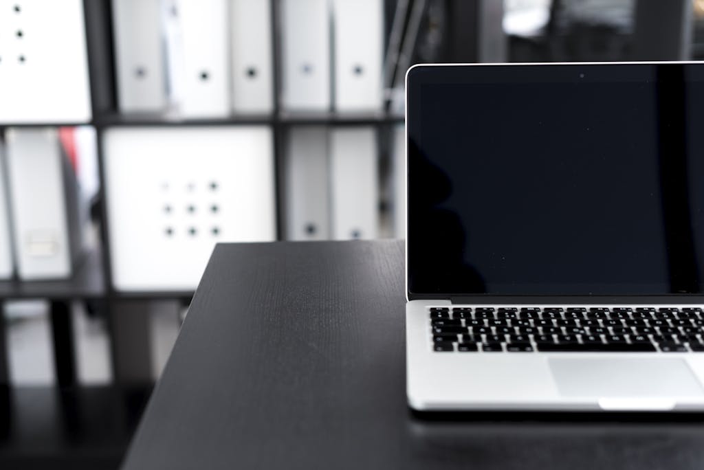 A sleek laptop on a desk in a modern office setting with organized shelves.
